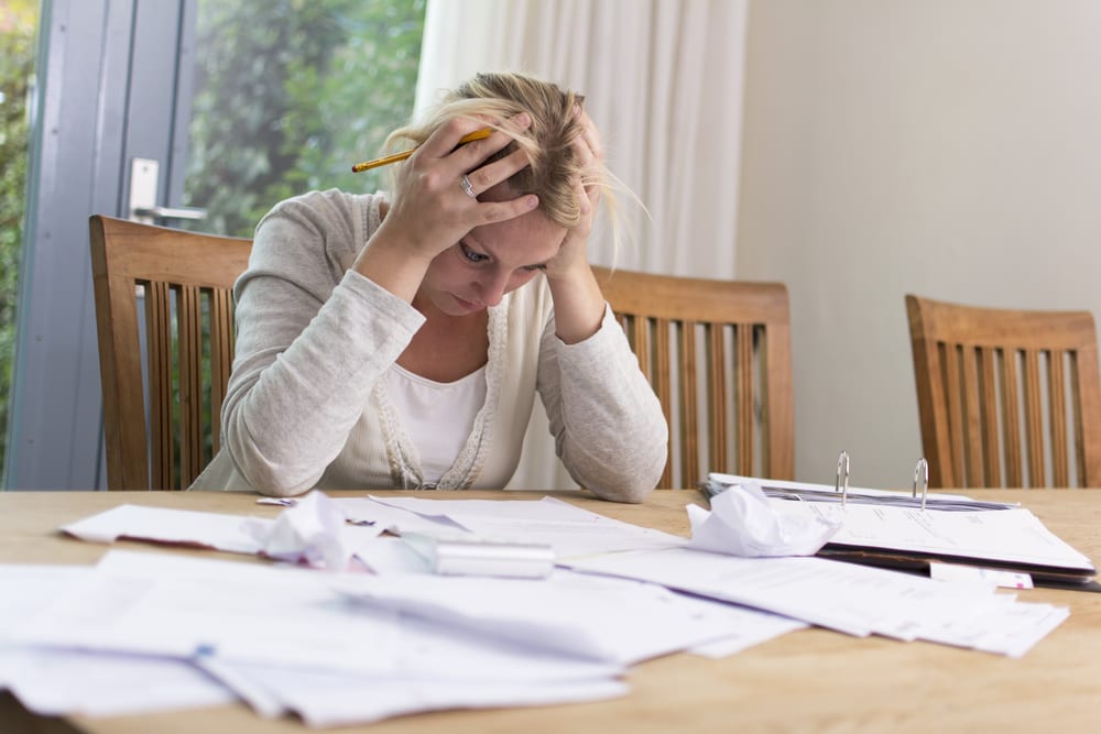 Woman sitting with hands on head looking at stacks of paperwork on table