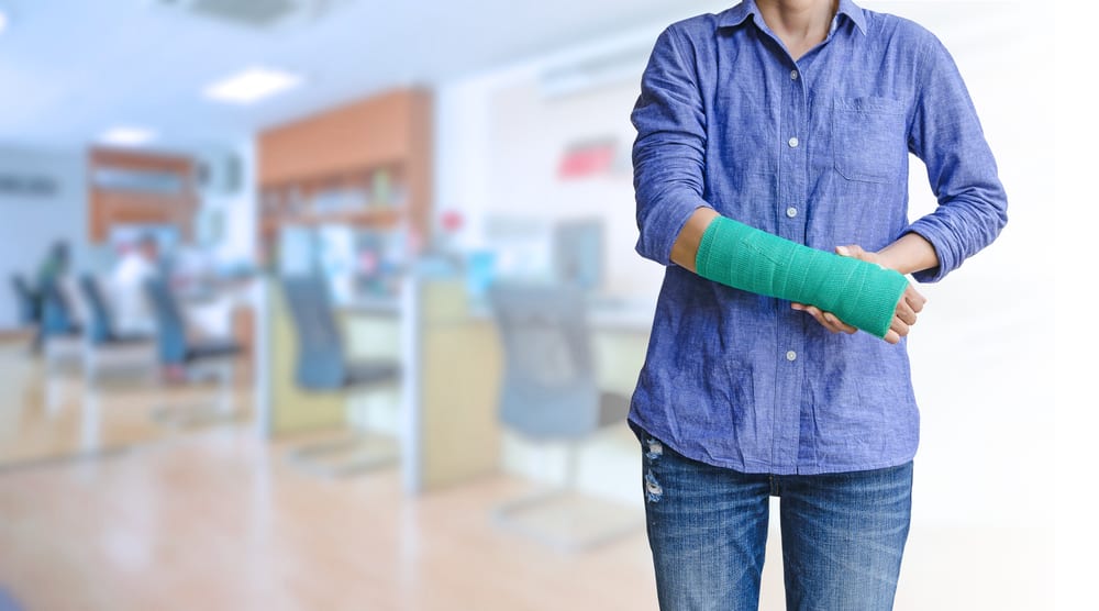 Woman in blue shirt and jeans with green arm cast standing in office space